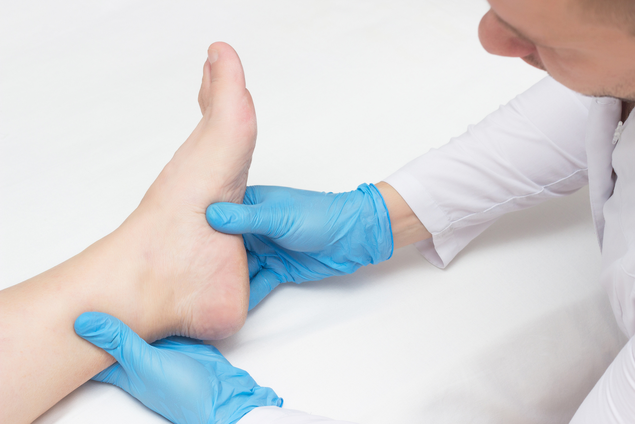 Doctor examines the patient's leg with heel spurs, pain in the foot, white background, close-up, plantar fasciitis
